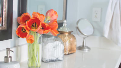 Bathroom countertop with soap, flowers in vase, jar of cotton balls, and mirror